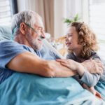 Small girl visiting ill grandfather in hospital room.